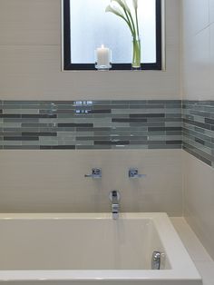 a white bath tub sitting under a window next to a vase with a flower in it