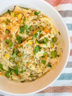 a white bowl filled with pasta and vegetables on top of a striped table cloth next to a fork