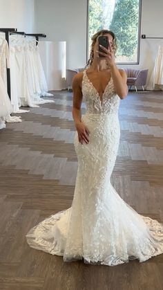 a woman taking a selfie in a wedding dress shop with her phone up to her face