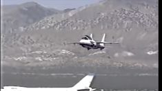 an airplane is flying low to the ground with another plane in the foreground and mountains in the background