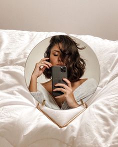 a woman laying in bed holding a cell phone to her face and looking at it