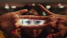 two hands making a heart shape with their fingers in front of the camera, while another hand is holding up an eye