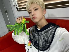 a young man holding up a green frog toy in his right hand while sitting on a red couch