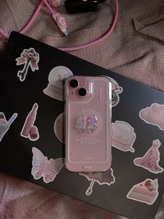 a pink phone case sitting on top of a bed next to a box with stickers