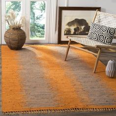 an orange and beige rug in a living room with a chair, potted plant and pictures on the wall