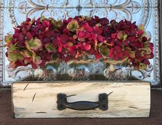 a vase filled with red flowers sitting on top of a wooden box next to a wall