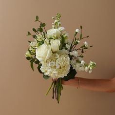 a bouquet of white flowers is held by someone's hand in front of a beige background