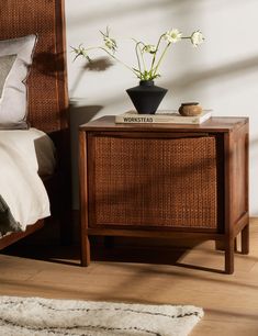 a nightstand with flowers on top of it next to a bed