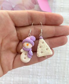 a hand holding two small snowmen and a christmas tree ornament on it's ear wires