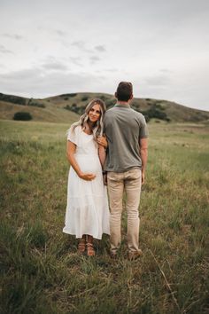 a pregnant woman standing next to a man in a field