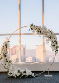 white flowers are arranged on a circular metal stand in front of a window overlooking the city