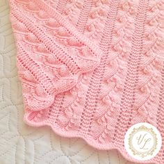 a pink knitted blanket sitting on top of a white quilted bed coverlet