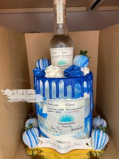 a blue and white cake in a cardboard box with a bottle of wine on top