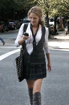 a woman is walking down the street while looking at her cell phone and wearing knee high boots