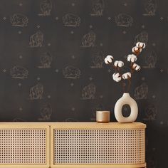 a vase with cotton flowers in front of a black wallpapered background and wooden cabinet