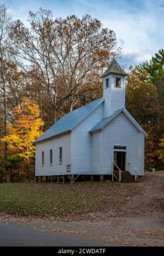 an old white church with a steeple surrounded by fall foliage and trees in the background