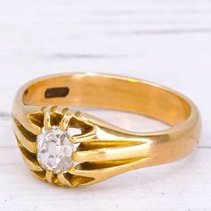 a gold ring with an old cut diamond in the center on a white wooden surface