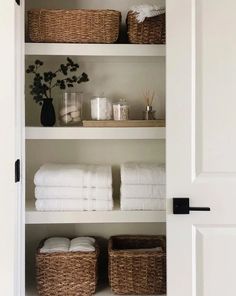 an open closet with towels, candles and baskets on the shelves in front of it