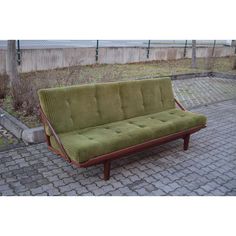 a green couch sitting on top of a brick floor next to a wooden frame fence