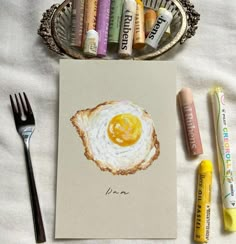 a card with an egg on it next to some crayons