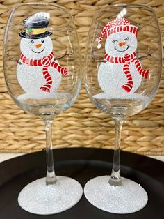 two wine glasses with snowmen painted on them sitting next to each other in front of a wicker basket