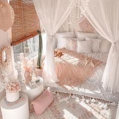 a white bed sitting next to a window covered in curtains and pink pillows on top of a rug