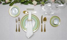 the table is set with gold and green plates, silverware, napkins, and wine glasses