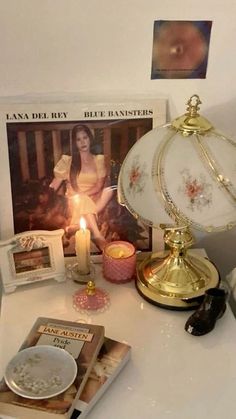 a table topped with books and candles on top of a white counter next to a lamp