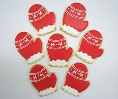 six decorated cookies in the shape of santa hats and mittens on a white surface