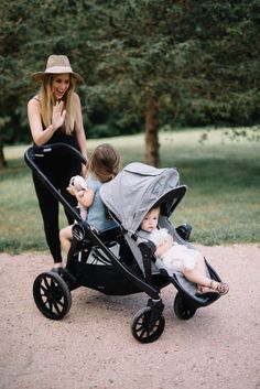 a woman standing next to a baby in a stroller and holding her hand up