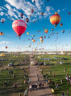 many hot air balloons are flying in the sky over a field with people walking on it