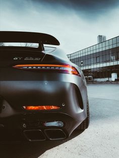 the rear end of a black sports car parked in front of a building with dark clouds