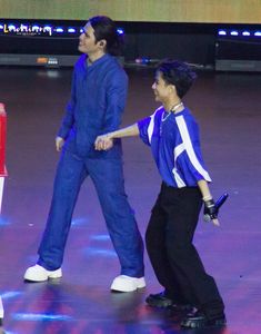 two people in blue jackets and black pants are walking on the ice with one person holding his hand