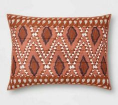 an orange and brown decorative pillow with diamonds on it's side, in front of a white wall