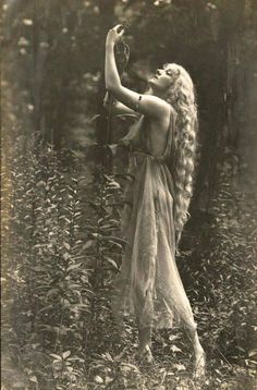 an old photo of a woman with long hair holding a bird in her hand while standing in the woods