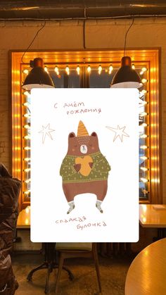 a poster with a bear wearing a hat and sweater in front of a lighted mirror