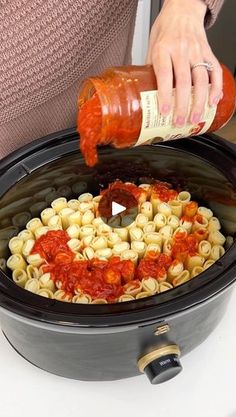 a person pouring sauce into a slow cooker filled with pasta