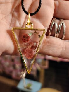 a hand holding a necklace with flowers in it and a triangle shaped pendant hanging from the bottom