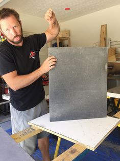 a man standing in front of a table holding up a piece of black tile on top of it