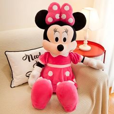 a minnie mouse stuffed animal sitting on top of a bed next to a pillow and lamp