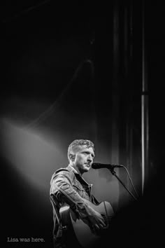 a man that is standing up with a guitar in front of him and singing into a microphone