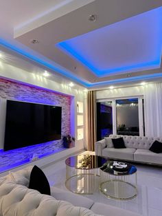 a living room with white couches and blue lights on the wall above them is lit up by recessed lighting