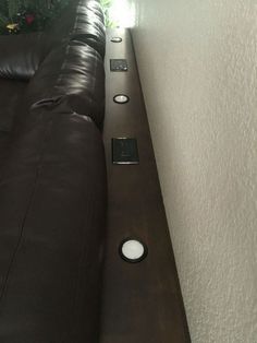 a black couch sitting next to a wall with two remote controls on it's side