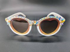 --🤍-»These beautifully embellished, one of a kind, hand decorated sunglasses have heart shaped inner, but round shaped outter frames. The lens is a warm yellowy brown that helps cancel the bright suns' rays. They have been decorated individually with white and gold iridescent rainbow sparkly rhinestones along the top. Each jewel has been individually double glued on with a cement glue for extra protection from wear and tear. **These come with a black microfiber drawstring pouch to keep these pr Decorated Sunglasses, Love Party, Face Jewels, Shaped Sunglasses, Heart Shaped Sunglasses, Party Festival, Drawstring Pouch, Gold Heart, Hand Decorated