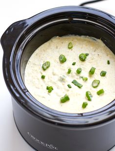 a crock pot filled with white sauce and green onions