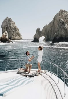 a man and woman standing on the bow of a boat in front of some rocks