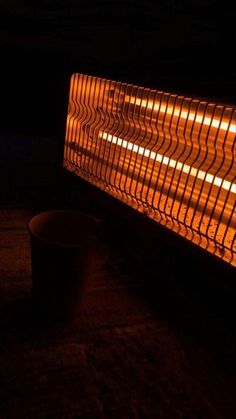 an orange colored heater sitting on top of a wooden table next to a cup