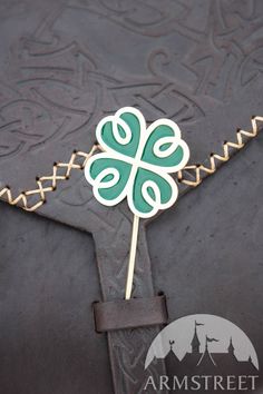 a green and white shamrock shaped pin on top of a black piece of paper with gold trim