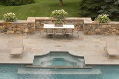 an outdoor pool with chairs and table next to the side walk way that leads to a stone wall