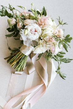 a bridal bouquet with white flowers and greenery on the back of a bow